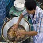 Tailandês frita frango colocando as mãos em óleo fervente