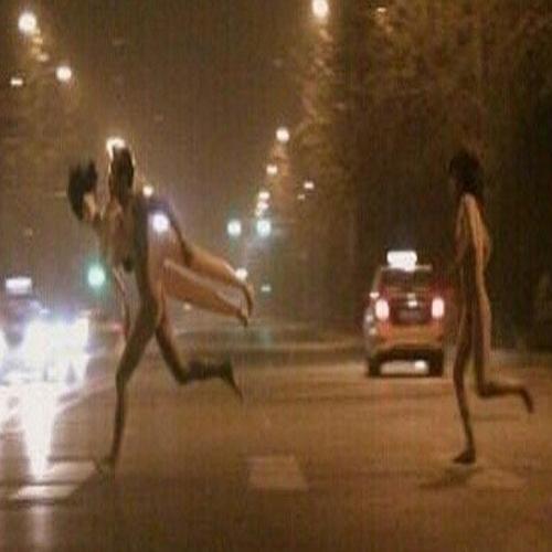 Homem e mulher nus correm com boneca inflável na rua